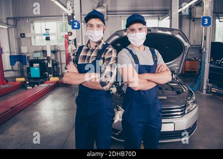 Two experts folded arms earing special safety outfit mask standing over background of entrance of automobile work station Stock Photo