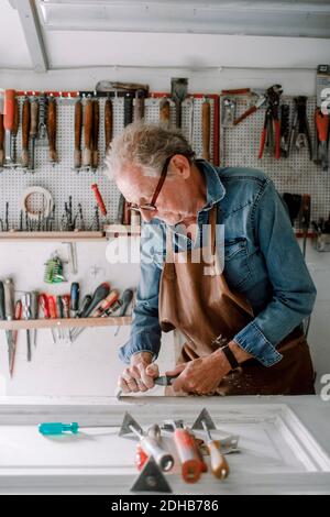 Senior male entrepreneur scraping window frame on workbench at store workshop Stock Photo