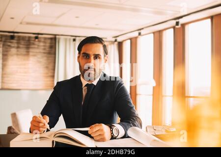 Portrait of confident lawyer with book sitting at table in law office Stock Photo