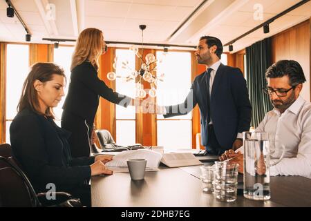 Male and female coworkers working while lawyers shaking hands at table in law office Stock Photo