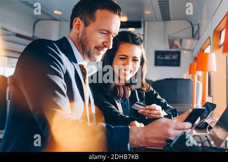 Happy businesswoman holding credit card while businessman using mobile phone at airport lobby Stock Photo