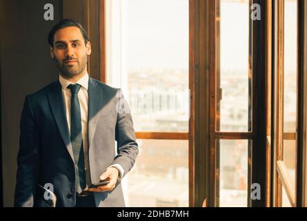 Portrait of confident male advisor standing by window at legal office Stock Photo