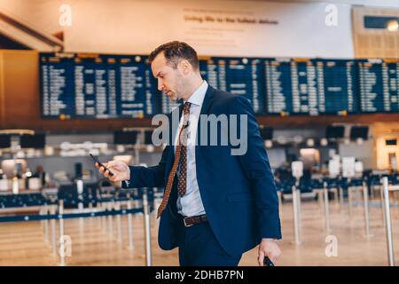 Mature businessman using mobile phone while walking in airport terminal Stock Photo