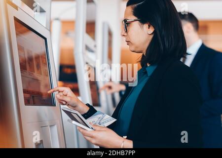 Side view of mid adult businesswoman using check in machine at airport Stock Photo