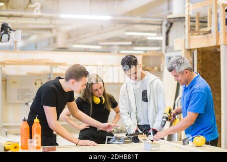 Male instructor explaining power drill on plank to trainees at workbench Stock Photo