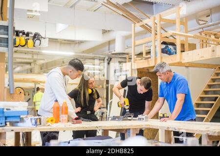Carpenter and trainees watching while man using power drill at workbench during training Stock Photo
