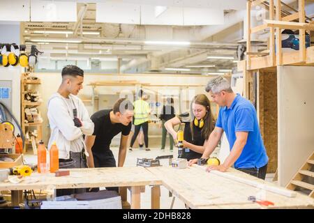 Male instructor and trainees watching while woman using power drill at workbench during training Stock Photo