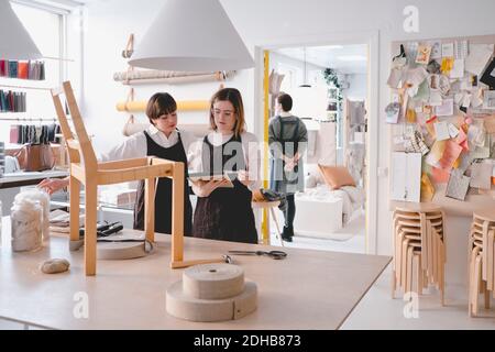 Female upholstery workers reading note pad with chair on desk in workshop Stock Photo