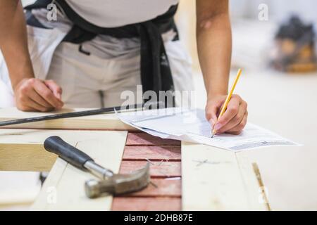 Midsection of young female trainee drawing on paper at workbench in illuminated workshop Stock Photo