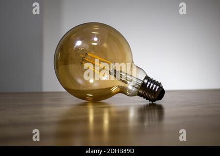 Big filament bulb with a yellow light on brown table. Large led lamps in retro style to the E27. Vintage style single lamp.