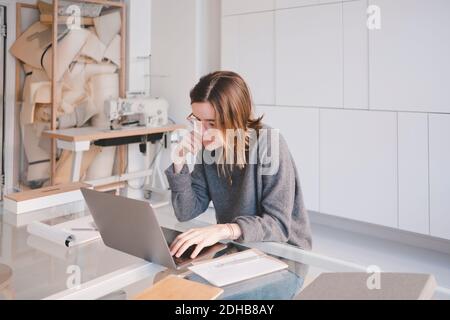 Young female fashion designer using laptop at desk in store Stock Photo