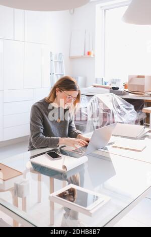 Young female owner using laptop at desk in workshop Stock Photo