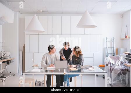 Female fashion designers discussing over laptop at desk in studio Stock Photo