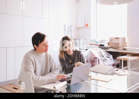 Female fashion designers discussing over laptop at desk in studio Stock Photo