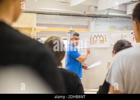 Confident male carpenter explaining over whiteboard to trainees in workshop Stock Photo