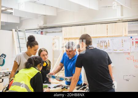 Male instructor using level amidst trainees at workbench in illuminated workshop Stock Photo