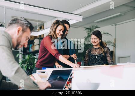 Smiling businesswoman working with colleagues while businessman using laptop in creative office Stock Photo