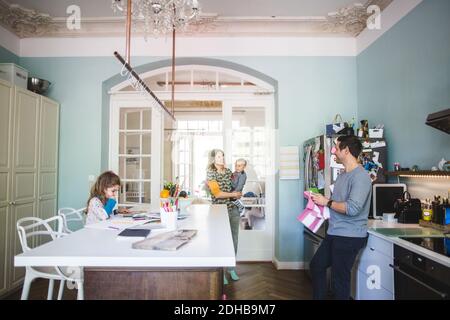Smiling woman carrying son while talking to man standing in kitchen at home Stock Photo