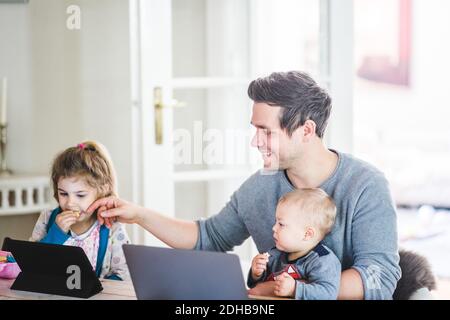 Smiling father sitting with son while touching girl watching movie on digital tablet at home Stock Photo