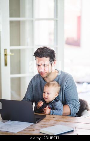 Man working on laptop while sitting with son at table Stock Photo