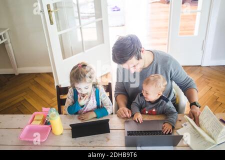 High angle view of smiling father with cute son sitting by daughter using digital tablet at table Stock Photo