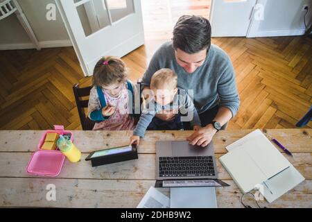 High angle view of man using laptop while sitting with cute son by daughter looking at digital tablet Stock Photo