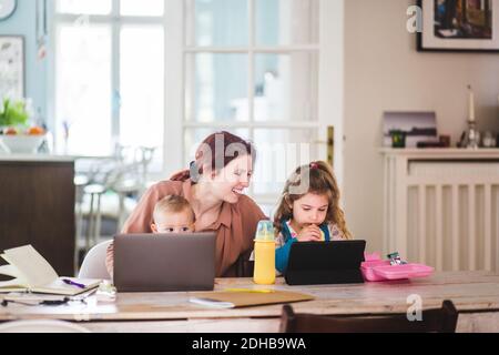 Smiling woman looking at girls watching movie on digital tablet while having food Stock Photo