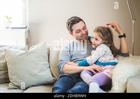 Smiling father with daughter sitting on sofa at home Stock Photo