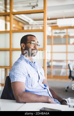 Thoughtful businessman looking away while sitting at desk in office Stock Photo