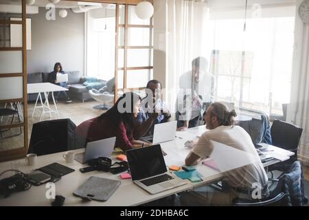 Male and female coworkers discussing in meeting at creative office seen through glass wall Stock Photo