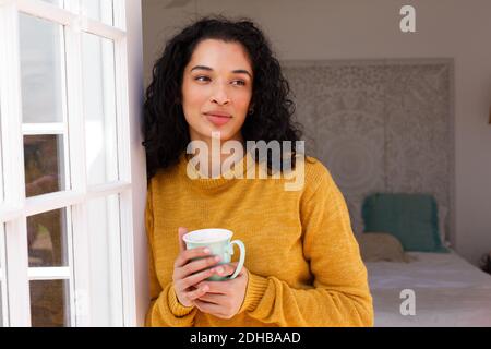 Smiling mixed race woman holding cup leaning and looking away Stock Photo