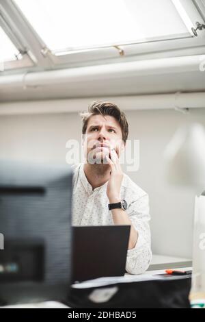 Thoughtful businessman looking away while sitting at desk in office Stock Photo