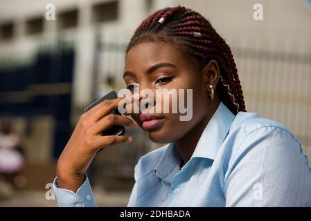 portrait of depressed young woman sitting outside with hand on nose holding a phone while thinking Stock Photo