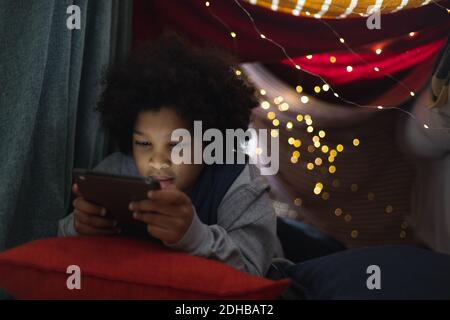 Mixed race girl lying in couch fort using digital tablet Stock Photo