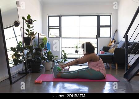 African american woman sitting on exercise mat working out. self isolation fitness at home during coronavirus covid 19 pandemic. Stock Photo
