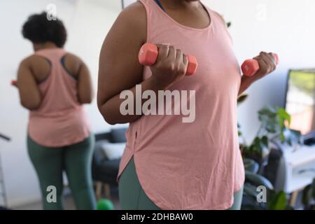Midesction of african american woman working out using dumbbells. self isolation fitness at home during coronavirus covid 19 pandemic. Stock Photo