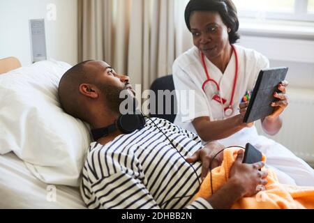 Female doctor showing digital tablet to young patient during visit in hospital ward Stock Photo