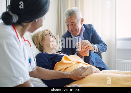 Senior man consoling female patient by doctor in hospital ward Stock Photo
