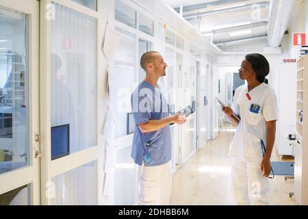 Male and female nurse discussing while standing in corridor at hospital Stock Photo