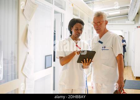 Male and female doctors discussing over digital tablet in hospital corridor Stock Photo