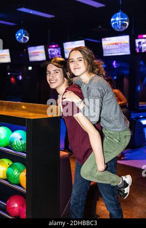 Portrait of smiling teenage boy giving piggyback ride to friend by rack at bowling alley Stock Photo