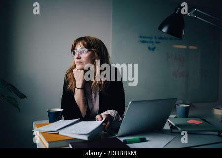 Thoughtful young businesswoman sitting with document and laptop at creative office Stock Photo