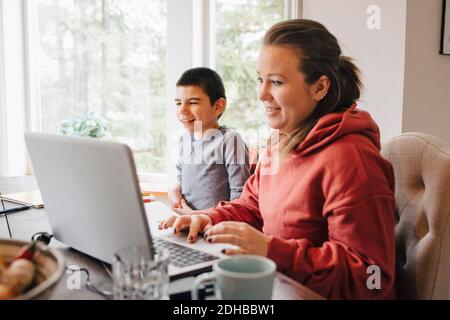 Mother using laptop on table while sitting with autistic son at home Stock Photo