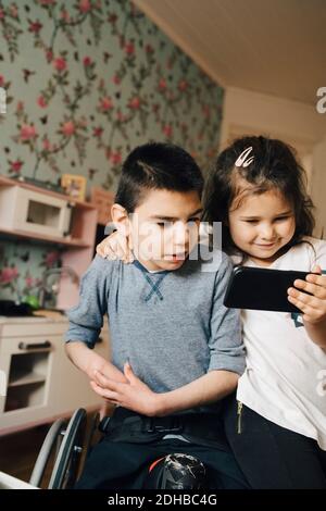 Sister showing video to autistic brother on smart phone at home Stock Photo