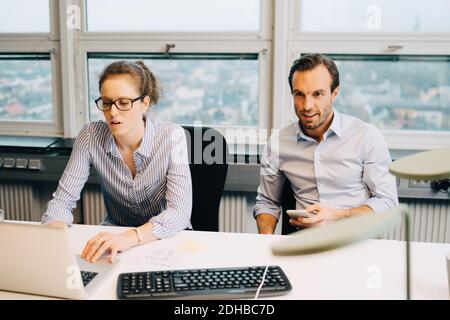 Colleagues working at desk against window in creative office Stock Photo