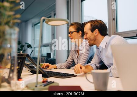 Smiling colleagues using laptop while sitting at desk in creative office Stock Photo