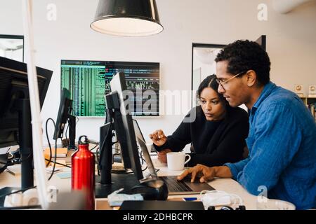 Focused male and female engineers coding over laptop on desk in office Stock Photo