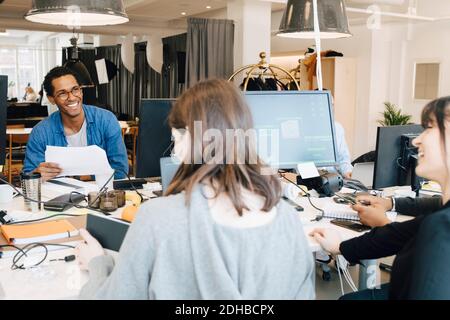 Cheerful male and female IT professionals talking while sitting at desk in creative office Stock Photo
