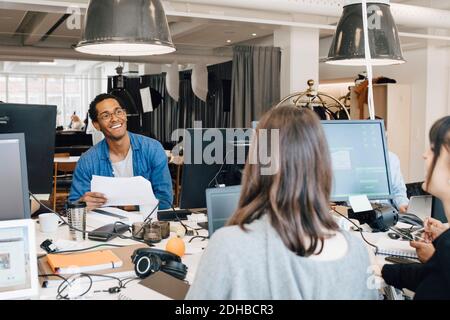 Cheerful multi-ethnic IT professionals talking while sitting at desk in creative office Stock Photo