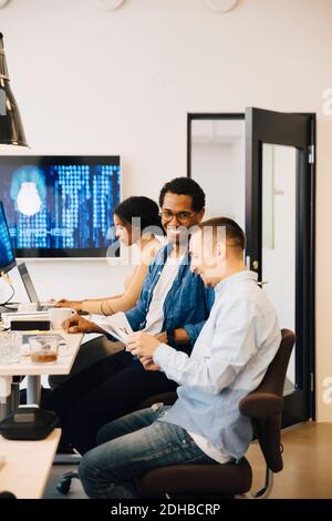 Male programmers discussing while female working in background at creative office Stock Photo